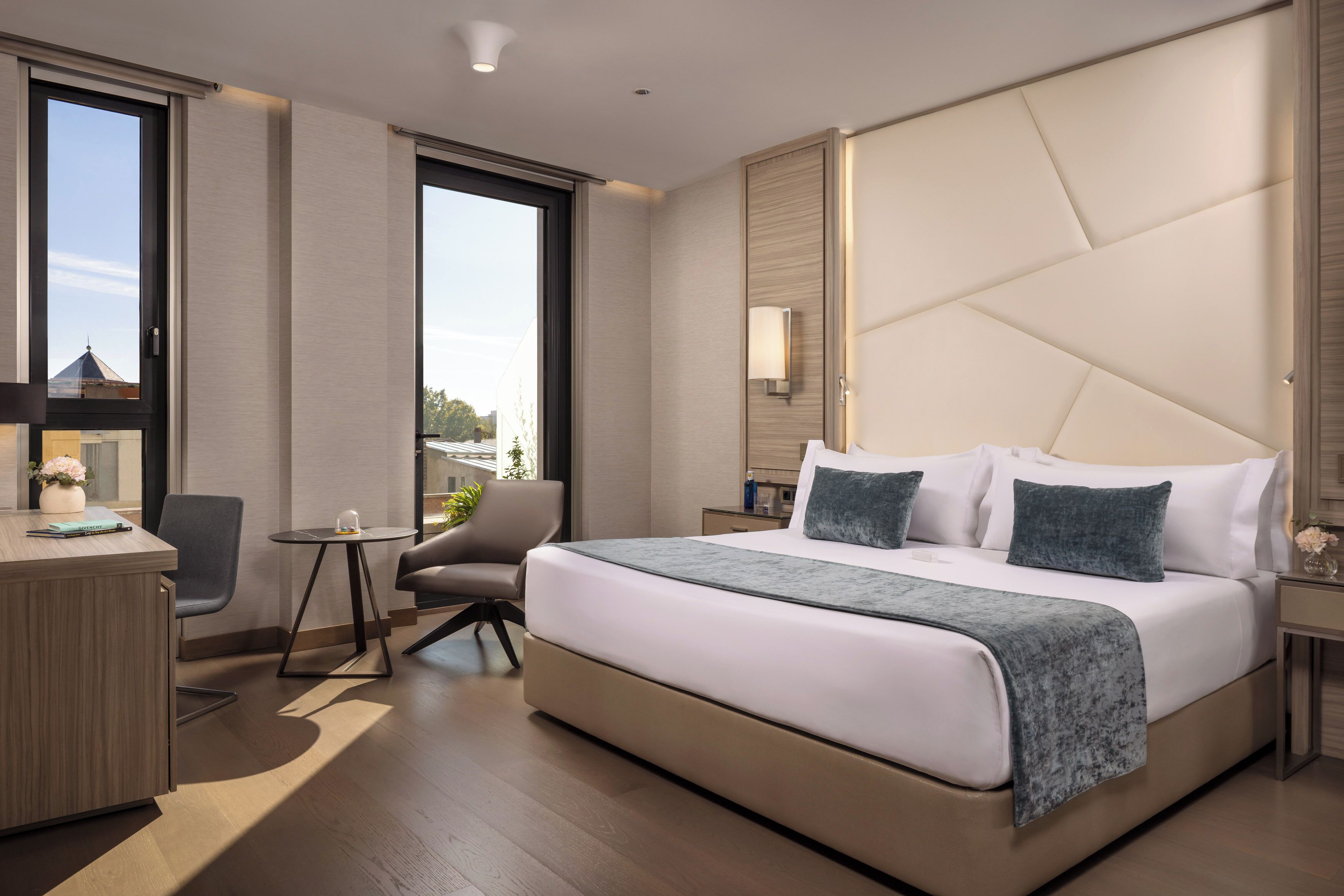 Una habitación de hotel moderna con una cama grande, un escritorio, una silla y una mesita.
