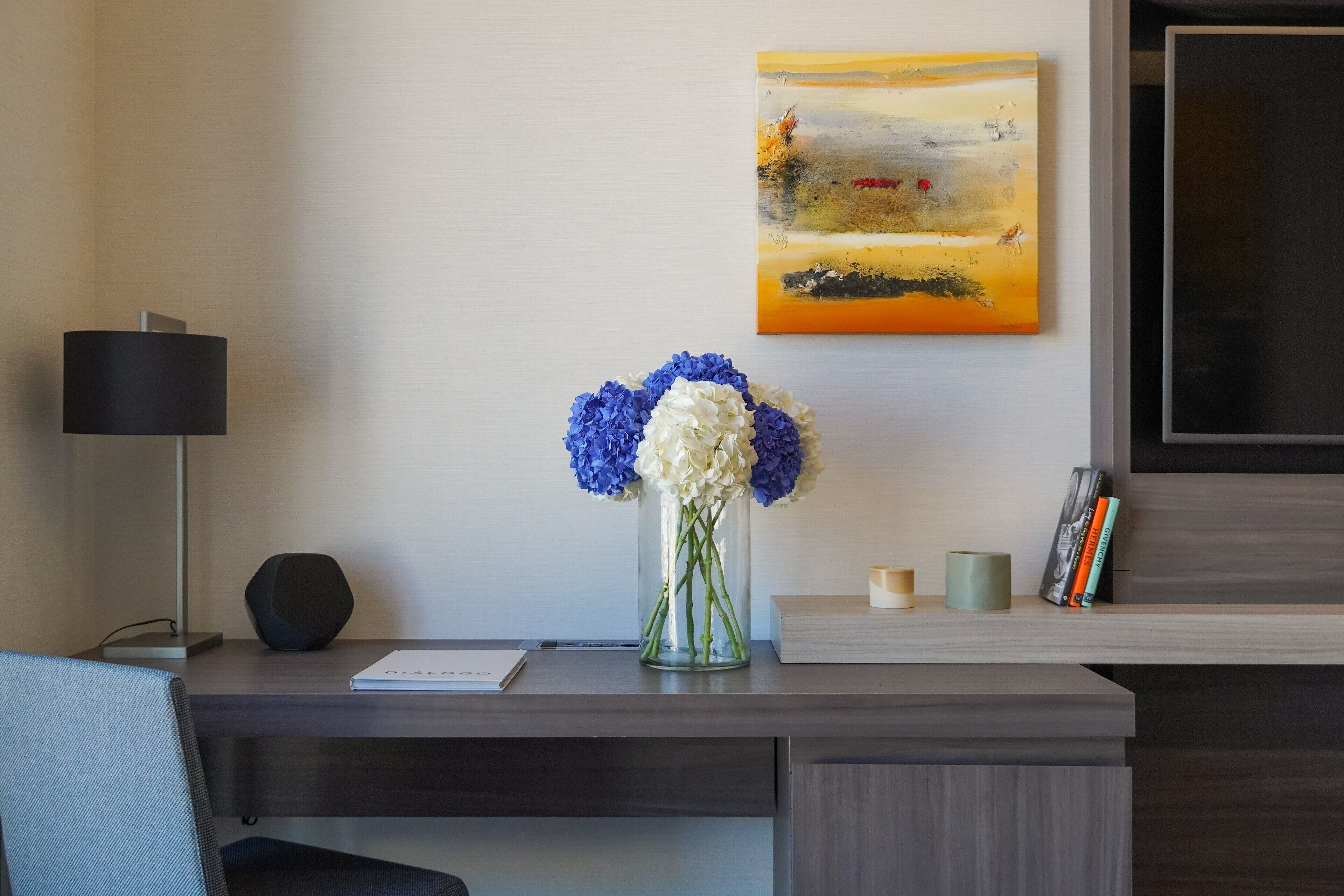 Un escritorio moderno con un jarrón de flores, una lámpara y un cuadro en la pared.