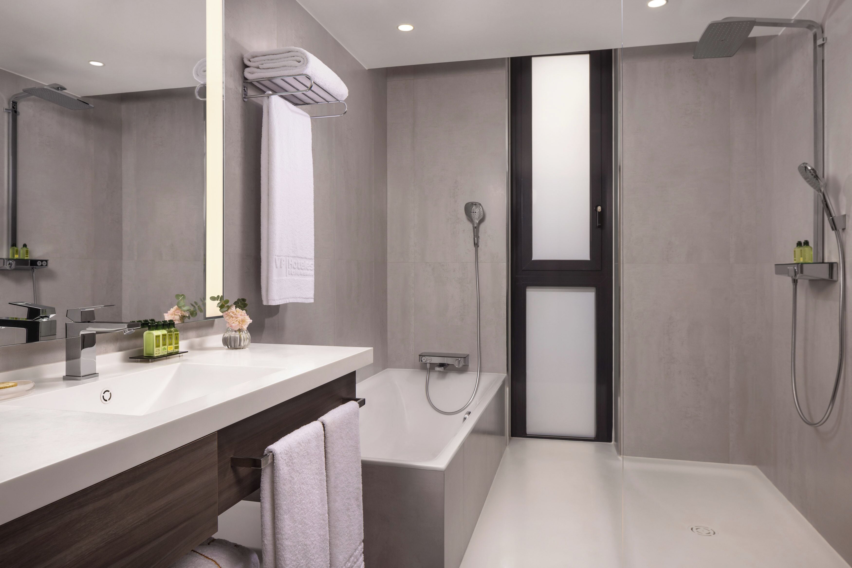 A modern bathroom with a white sink, a large mirror, a shower, and a dark door.