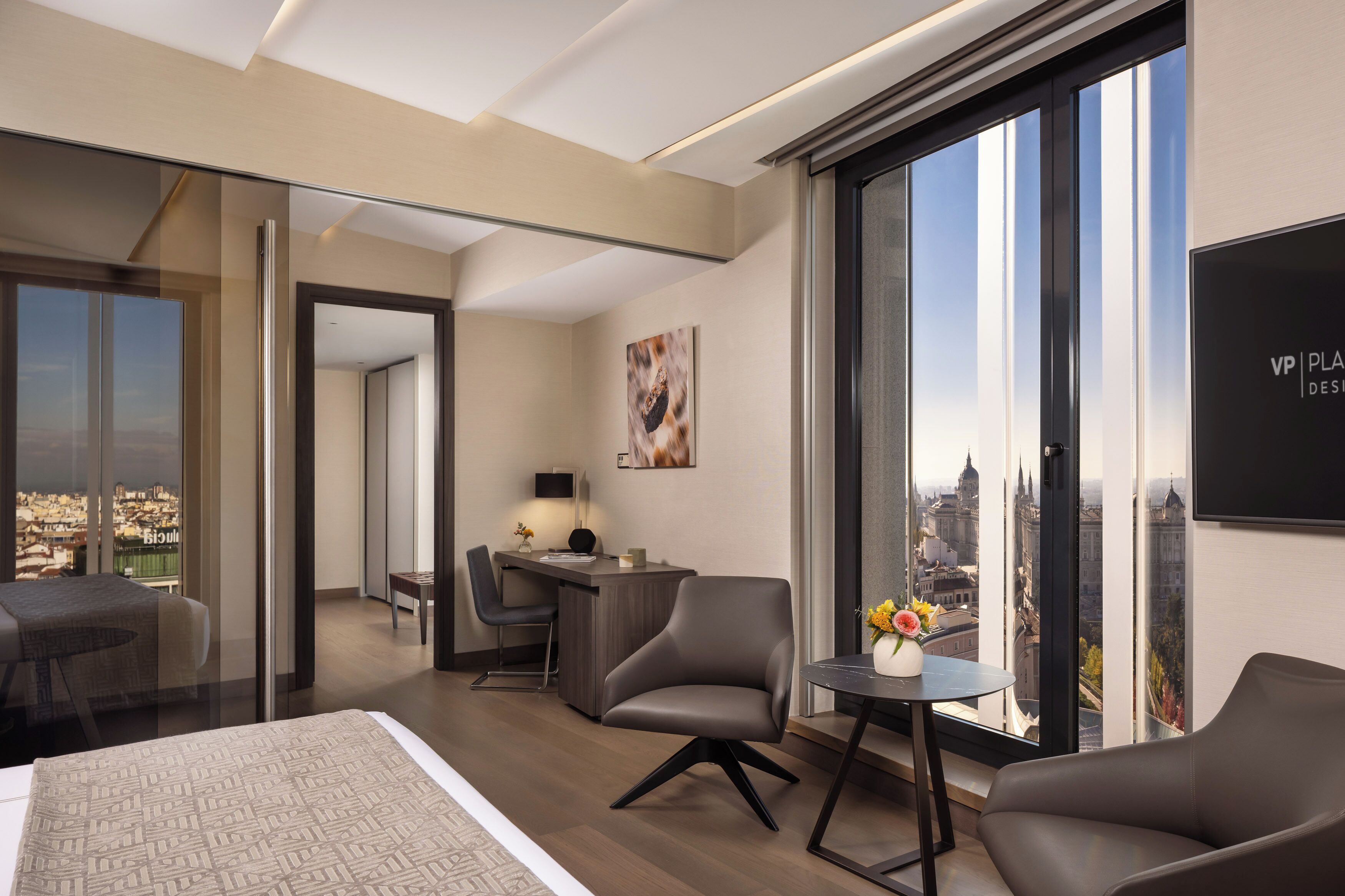 Ein modernes Hotelzimmer mit einem großen Bett, einem Schreibtisch, zwei Stühlen und einem kleinen Tisch mit Blumen.