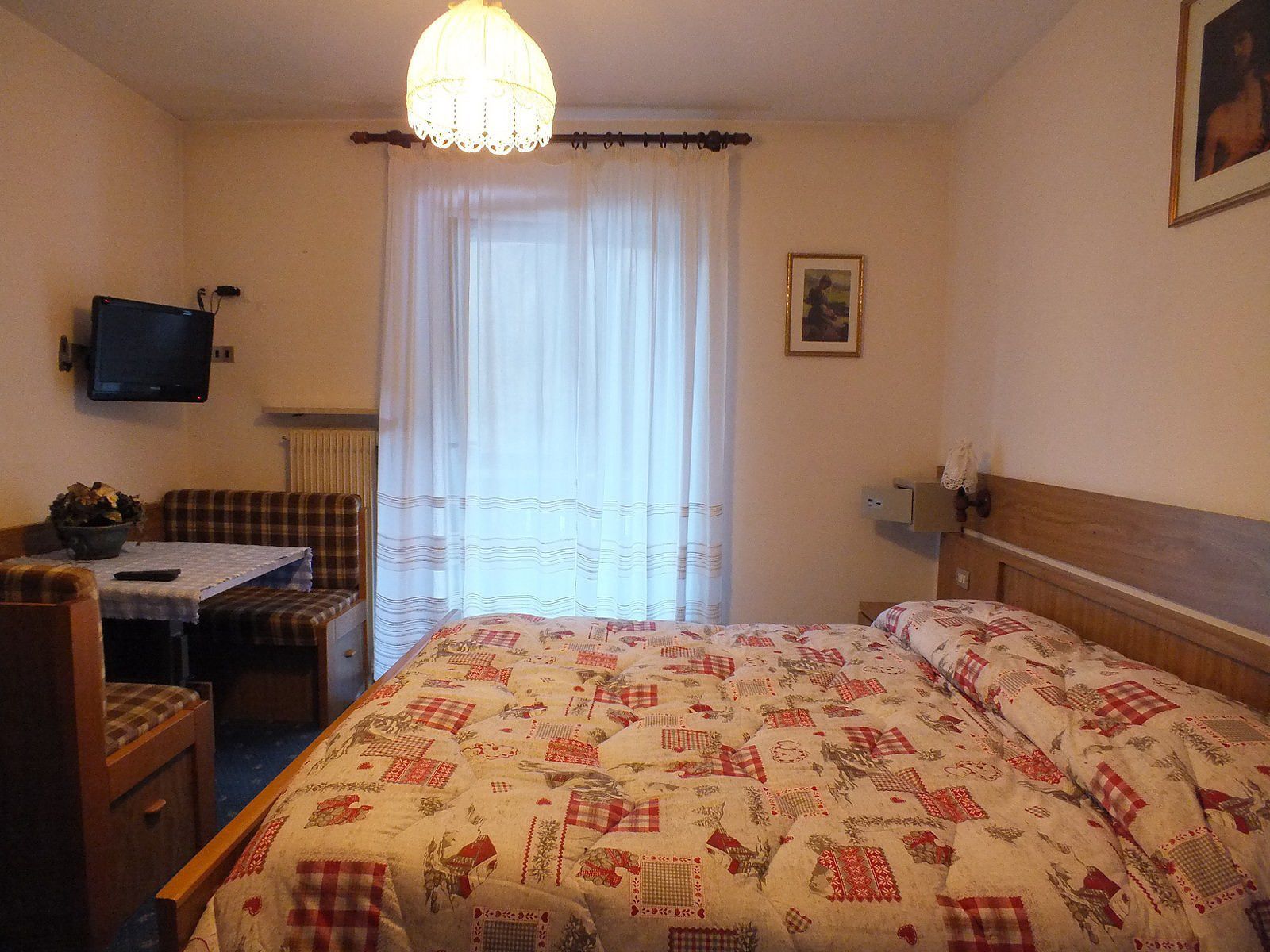 A bedroom with a bed, a desk, a chair, a television, and a window with curtains.