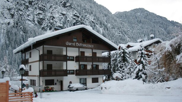 A multi-story building named "Garnier De Francesco" with balconies, surrounded by snow-covered trees and mountains. - Albergo Garni Defrancesco (Campitello di Fassa)