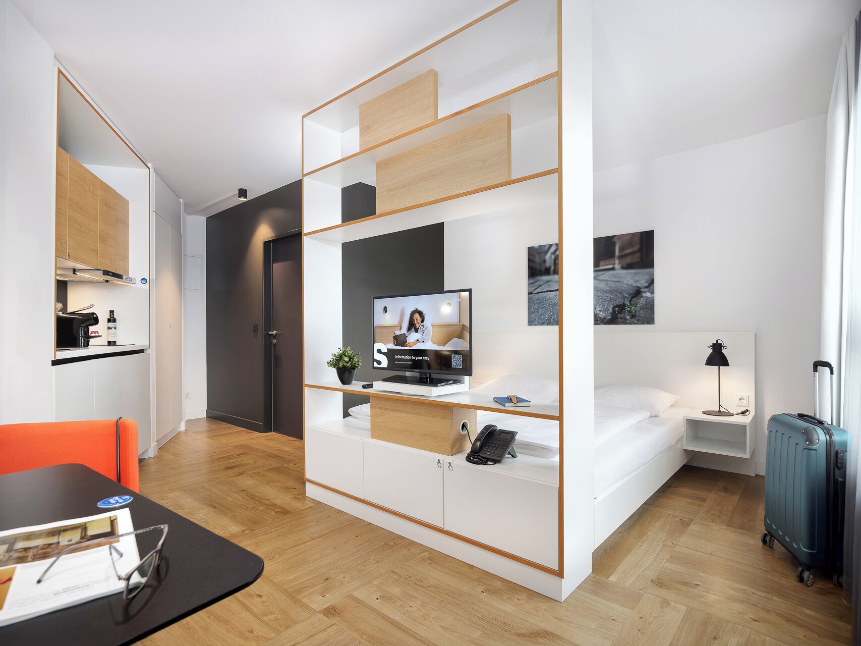 A modern hotel room with a bed, a desk with a computer, a television, and a small bedside table.