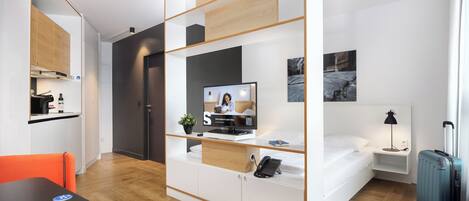 A modern hotel room with a bed, a desk with a computer, a television, and a small bedside table.