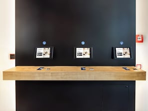 Un comptoir d’accueil doté de trois écrans numériques affichant des informations, un comptoir en bois et un mur noir.