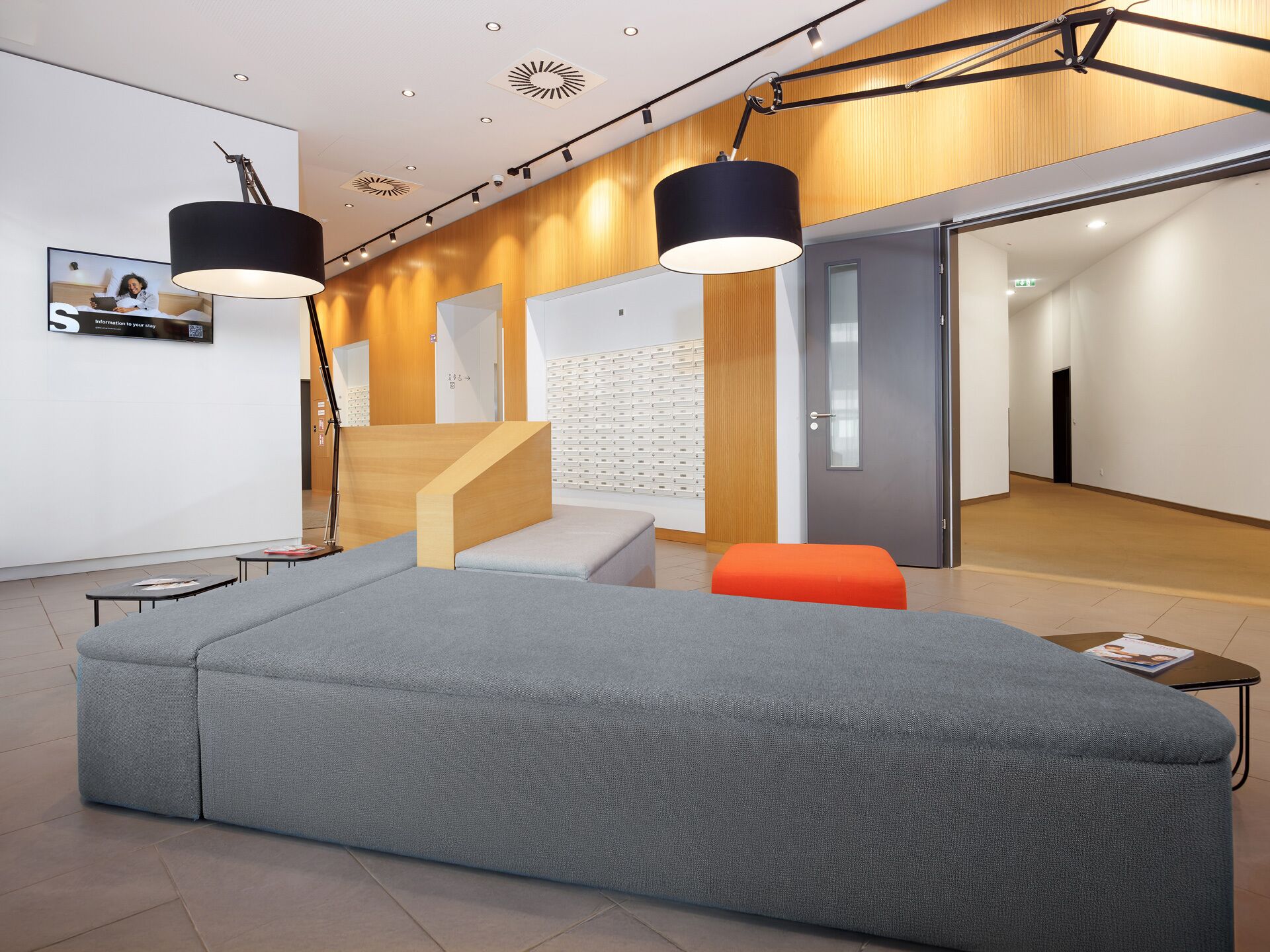A modern waiting area with a large grey sofa, a wooden reception desk, and a staircase leading to another level.