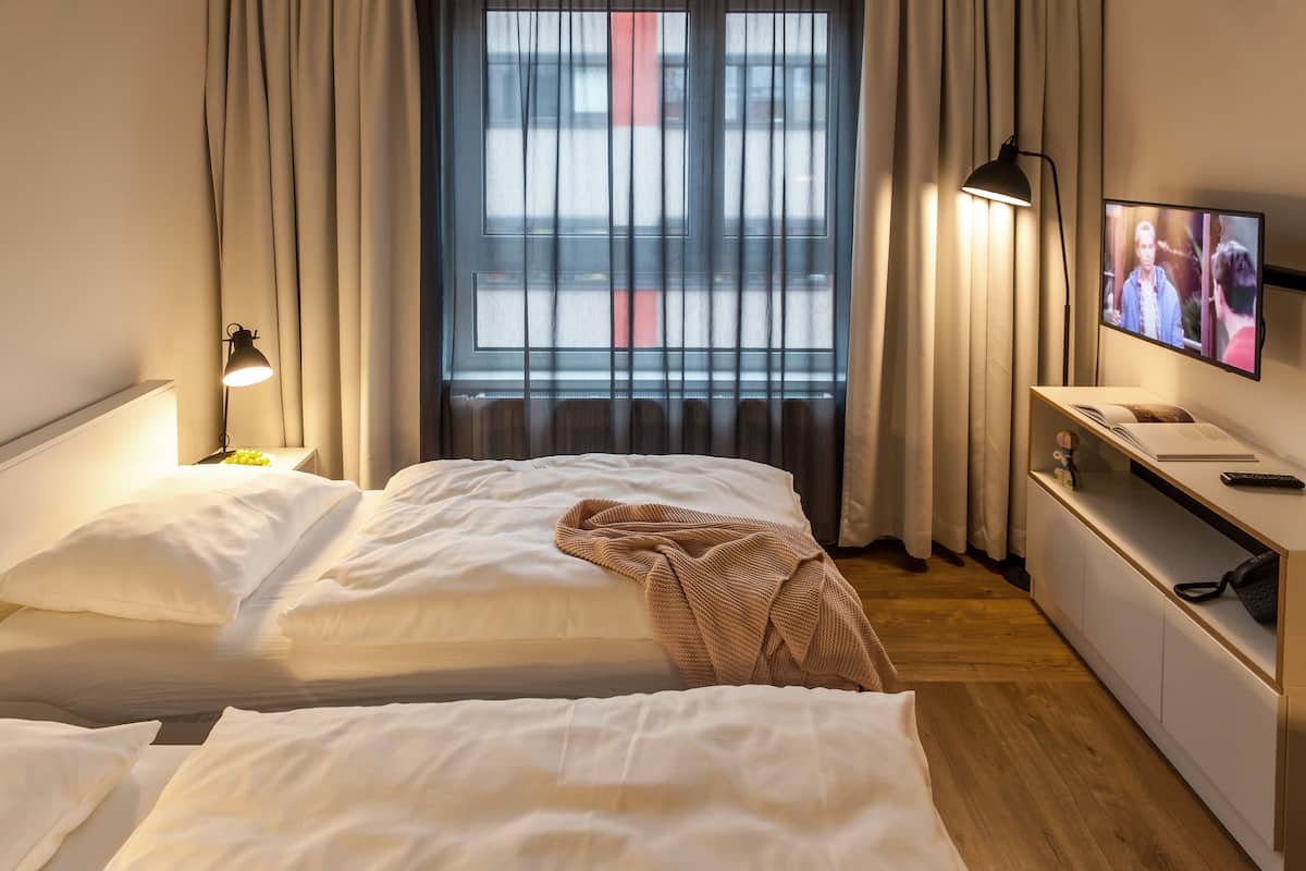 Une chambre d’hôtel avec deux lits, une télévision, une lampe de chevet et une fenêtre avec des rideaux.