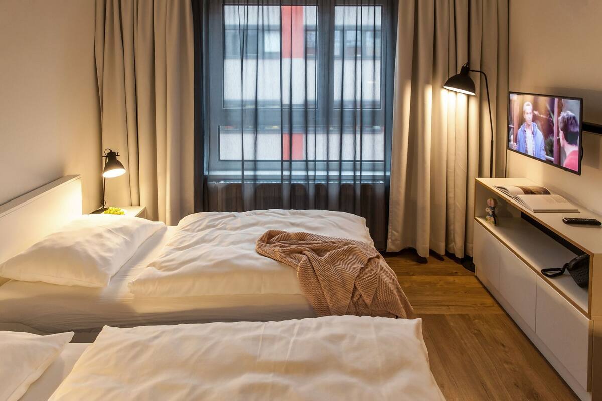 Une chambre d’hôtel avec deux lits, une télévision, une lampe de chevet et une fenêtre avec des rideaux.