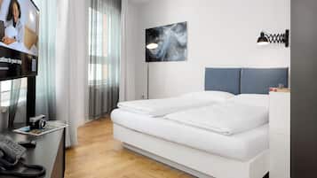 A modern hotel room with a bed, a desk with a phone, a TV, and a painting on the wall.