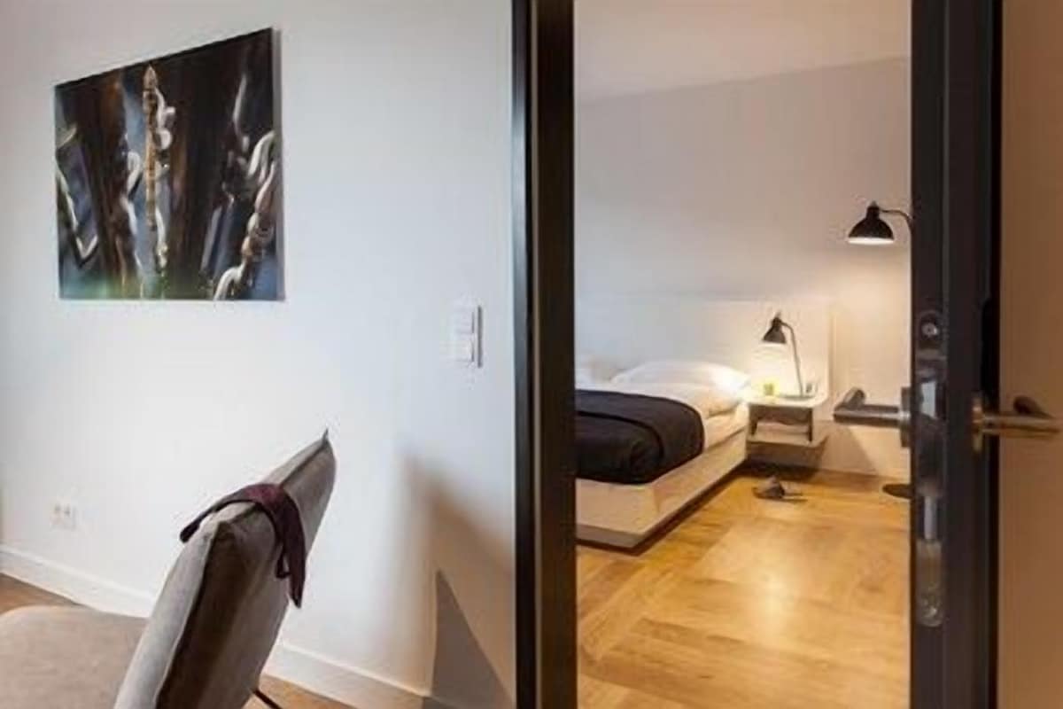 Een moderne slaapkamer met een bed, nachtkastje, lamp en een stoel.