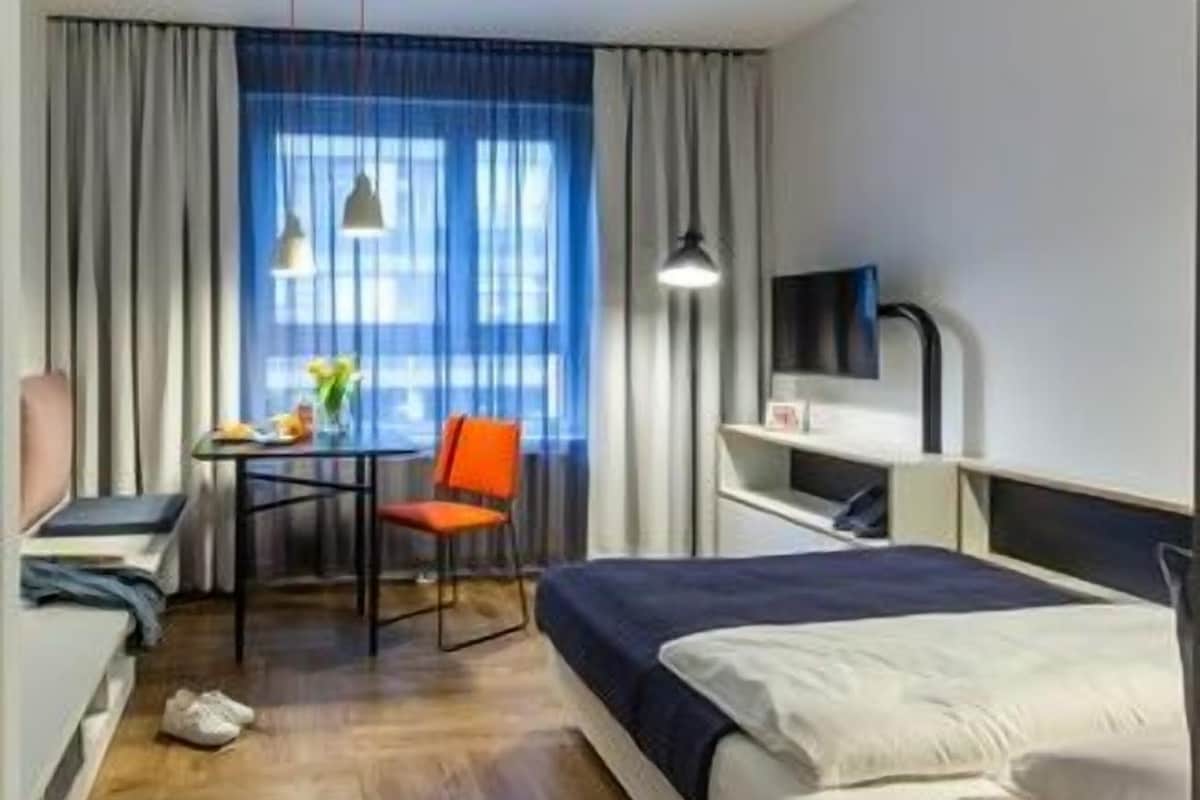 Een hotelkamer met een bed, een bureau, een stoel, een televisie en gordijnen.