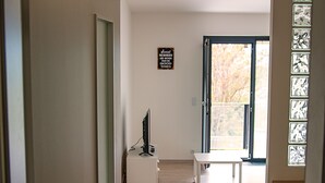 A hallway with a wooden floor, a white bench, and a television on a stand. - Trinity Residence (Prague)