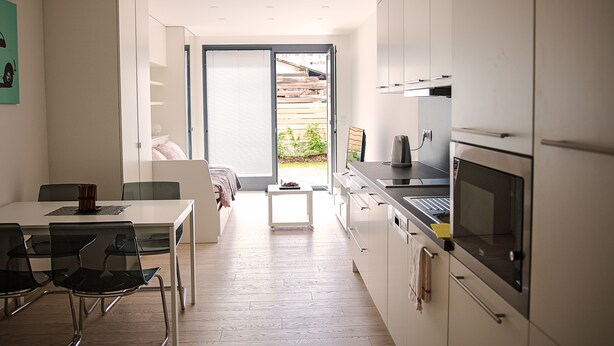 A modern kitchen with white cabinets, a dining area with a table and chairs, and a sliding glass door leading to an outdoor area. - Trinity Residence (Prague)