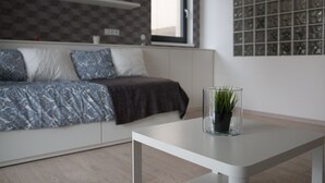 A modern living room with a sofa, a glass table with a plant, and a window with a geometric patterned wall. - Trinity Residence (Prague)