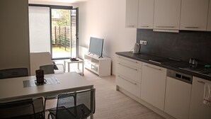 A modern kitchen with a dining area, a TV on a small table, and a sliding glass door leading to a garden. - Trinity Residence (Prague)