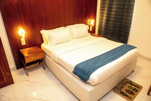 Una cama bien hecha con una manta azul, mesitas de noche de madera con lámparas y un felpudo con motivos de cactus.