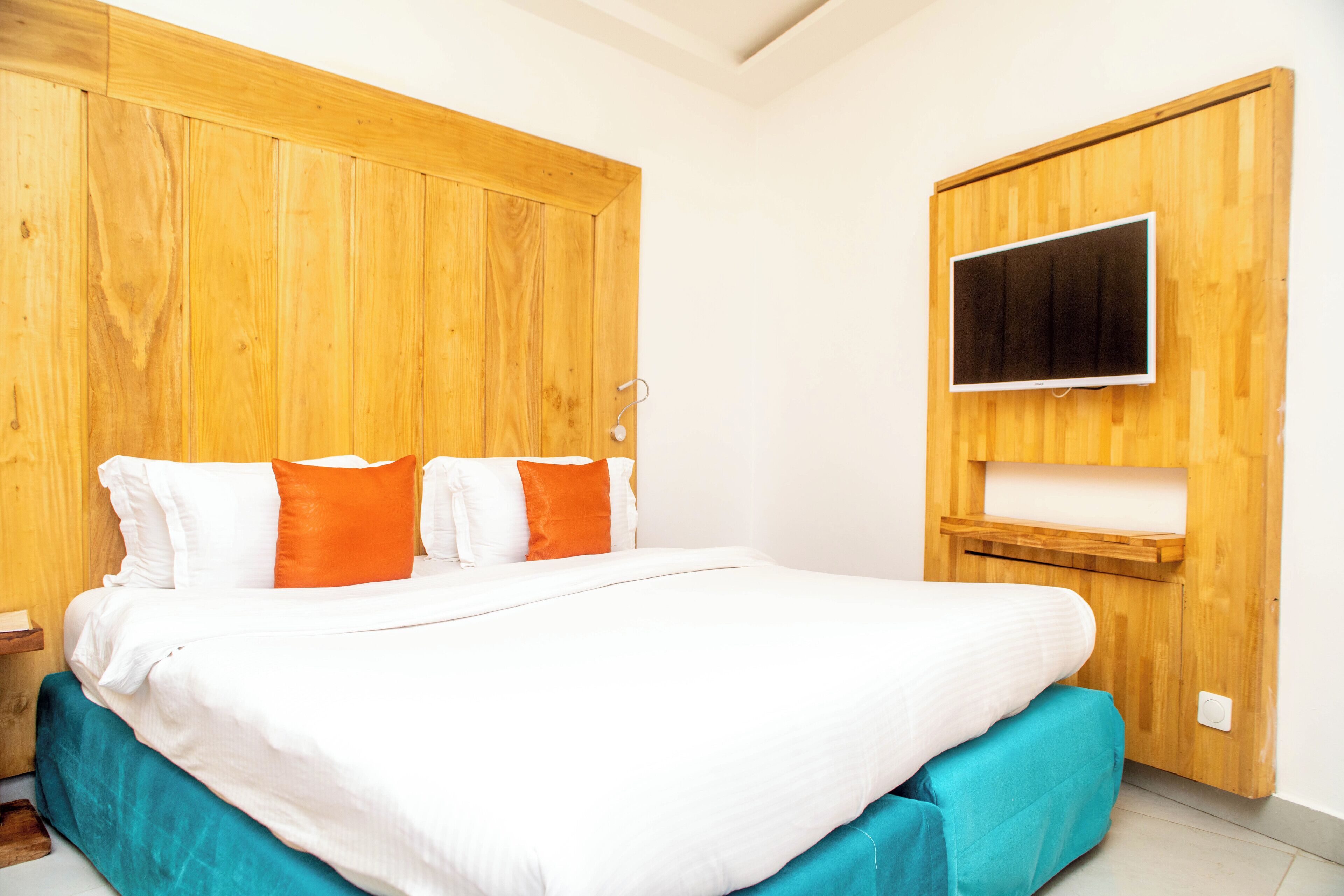 A bedroom with a wooden headboard, a bed with white and orange bedding, and a mounted TV on the wall.
