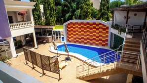 Una piscina con un muro a cuadros, muelle de madera y una escalera que sube a un balcón.