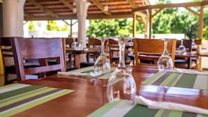 Un restaurante con mesas y sillas de madera, cristalería transparente y manteles individuales a rayas verdes.