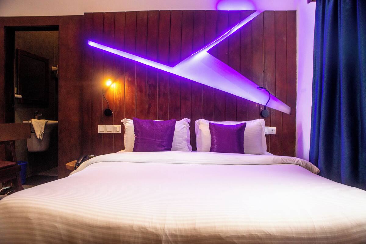 Une chambre d’hôtel avec un lit, des murs recouverts de panneaux en bois, un luminaire fixé au mur et une salle de bain visible au fond.