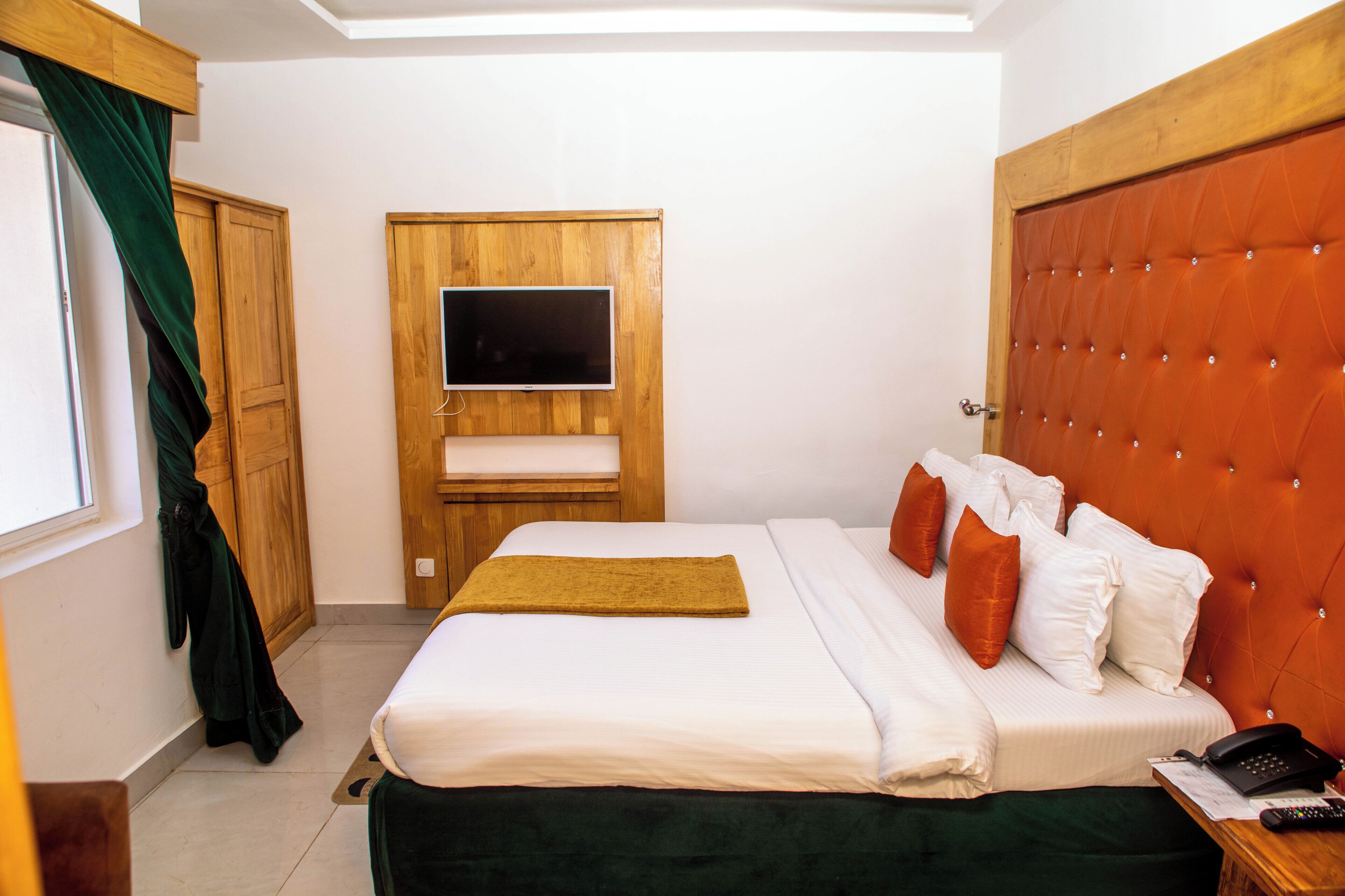 Una habitación de hotel con una cama, un televisor fijado a un panel de madera, un armario y una mesita de noche con un teléfono.