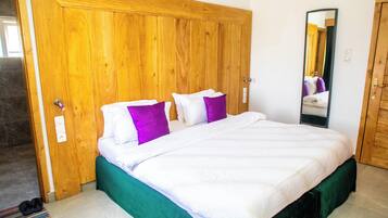 Un dormitorio con un armario de madera, una cama con ropa de cama blanca y morada, y un espejo en la pared.