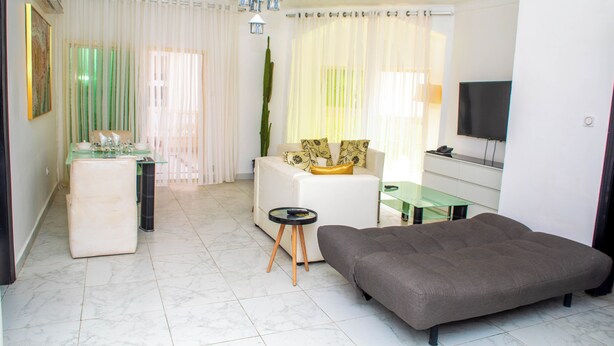 Una sala de estar moderna con sofá, una mesa de centro de vidrio, televisor y comedor con mesa y sillas de vidrio.