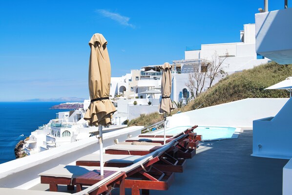 Une terrasse sur le toit, dotée de chaises longues et de parasols, offrant une vue sur la mer.