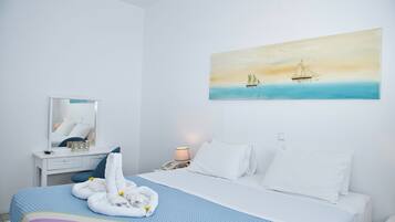 A hotel room with a bed, a desk, a chair, a mirror, a painting of a sailboat, and a lamp.