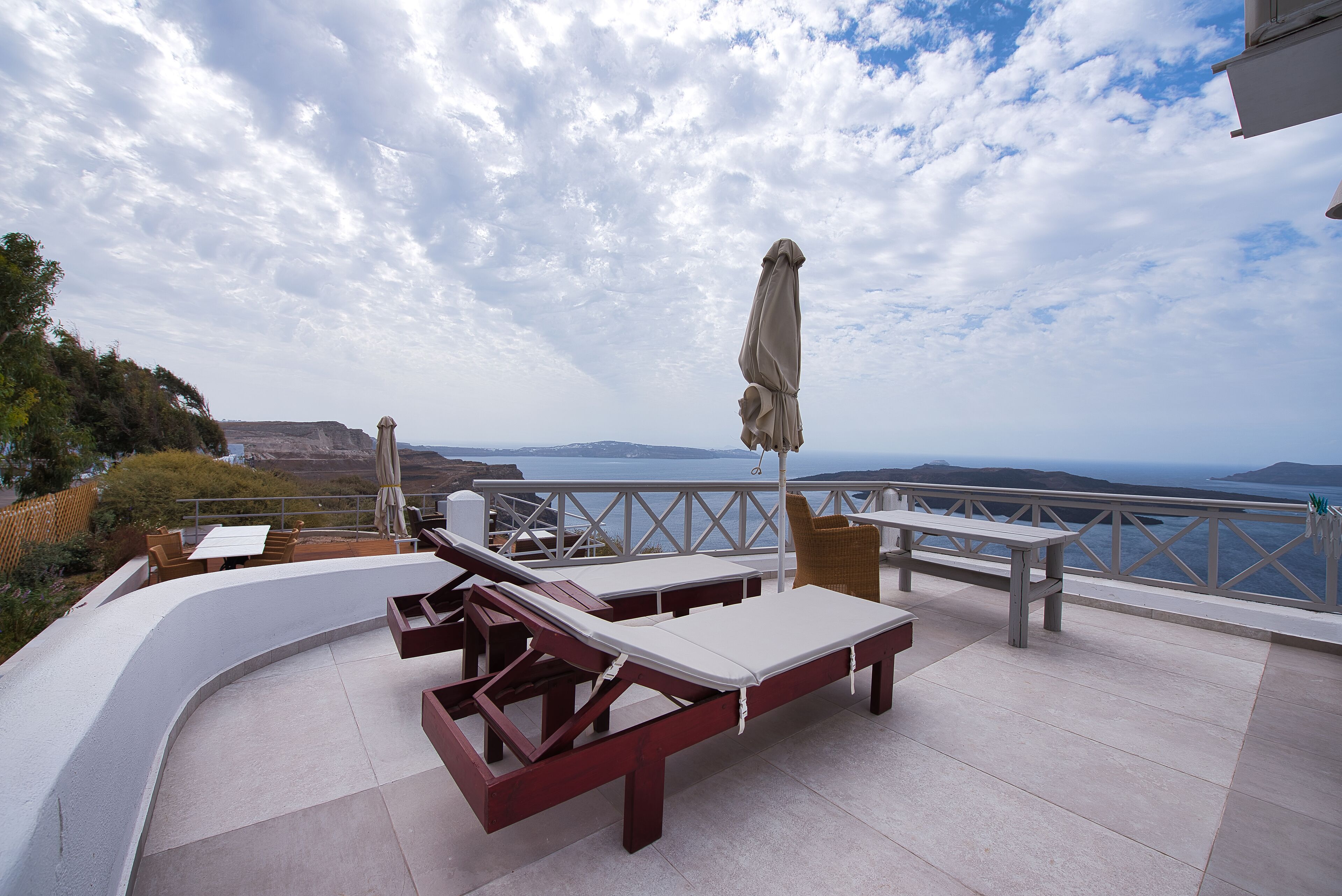 A terrace with lounge chairs and a table, overlooking a scenic coastline.