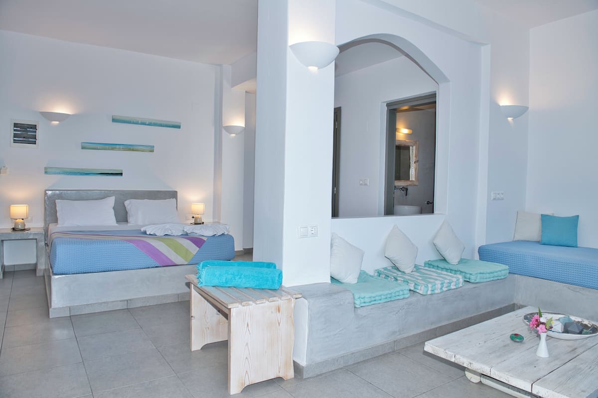 Una habitación de hotel moderna con una cama grande, un sofá, una mesita de centro y una pequeña mesa con un jarrón.