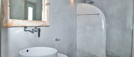 A bathroom with a round sink, a mirror, a shower, and a toilet.