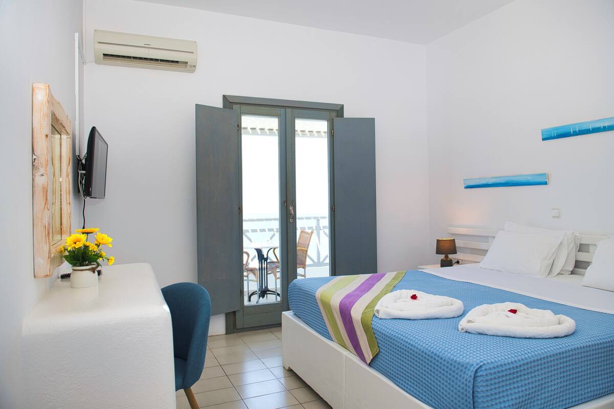 Una habitación de hotel con cama, escritorio, silla, televisor y balcón con sillón.