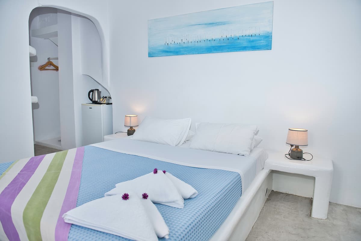 Habitación de hotel con cama, dos mesitas de noche con lámparas, un cuadro en la pared y un pasillo con un perchero.