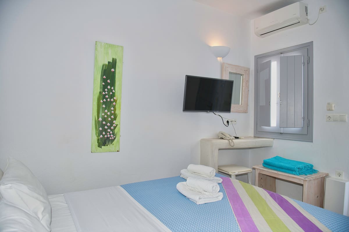 Habitación de hotel con cama, televisión montada en la pared, ventana y una mesita con una toalla y una manta.