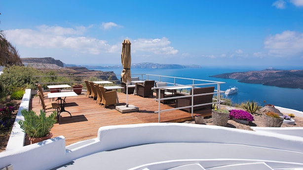 Eine Holzterrasse mit Gartenmöbeln, einem weißen Geländer und Blick auf das Meer und die Klippen.