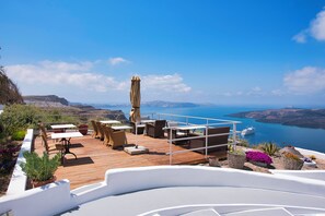 Une terrasse en bois, dotée de mobilier d’extérieur, d’une rambarde blanche et offrant une vue sur la mer et les falaises.