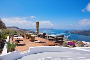 Una terraza de madera con mobiliario exterior, barandilla blanca y vistas al mar y a los acantilados.