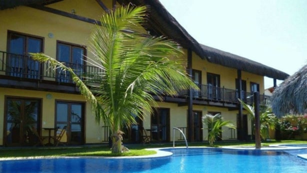A hotel with a swimming pool, a thatched roof, and a well-maintained lawn. - Sirius Canoa Residencial (Aracati)