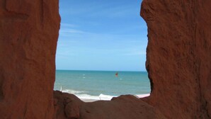 A natural rock formation framing a beach view with clear blue sky and ocean. - Sirius Canoa Residencial (Aracati)