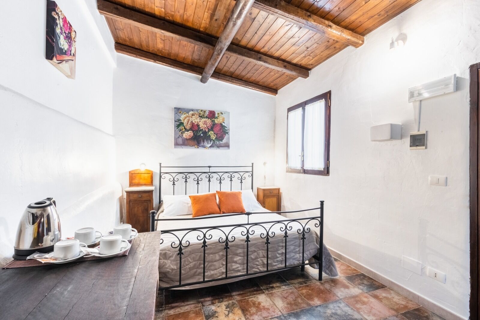 A bedroom with a metal bed frame, a wooden ceiling, a painting on the wall, and a tiled floor.