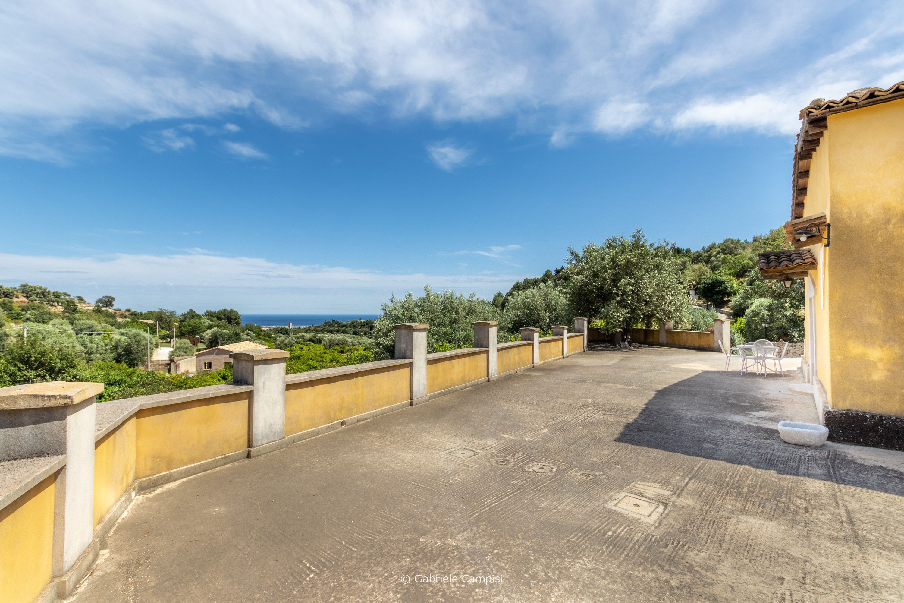 A rooftop terrace with a view of the sea and greenery.