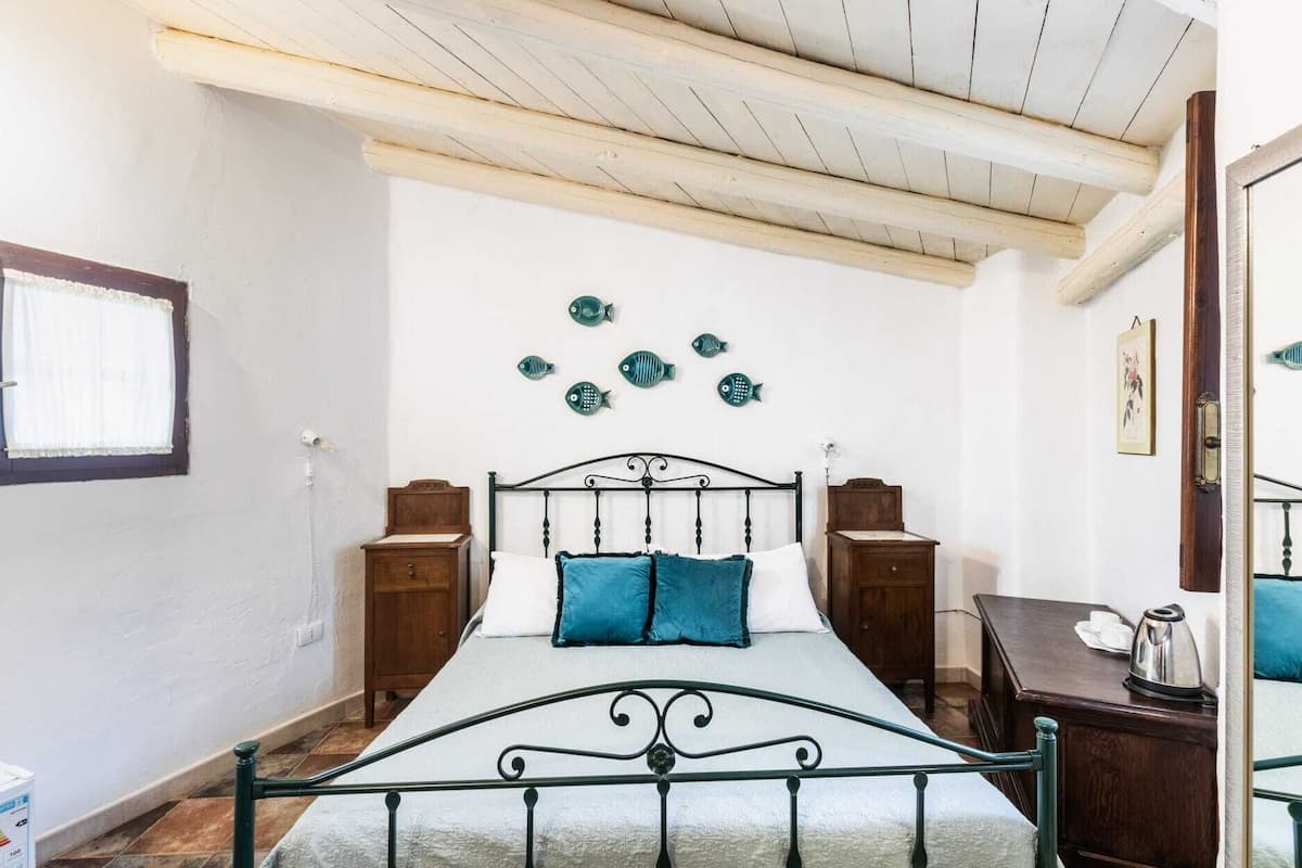 Een slaapkamer met een bed, houten nachtkastjes, een kapstok, een raam met gordijnen en decoratieve visdecoratie aan de muur.