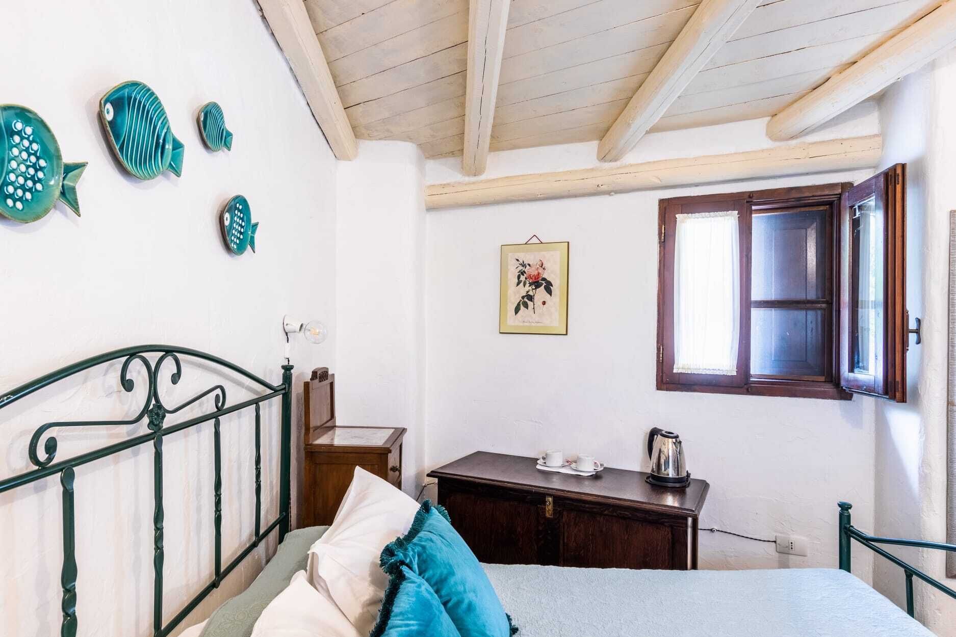 A bedroom with a bed, a wooden nightstand, a dresser, a window with a wooden frame, and a wall with decorative fish and a framed picture.