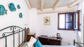 A bedroom with a bed, a wooden nightstand, a dresser, a window with a wooden frame, and a wall with decorative fish and a framed picture.