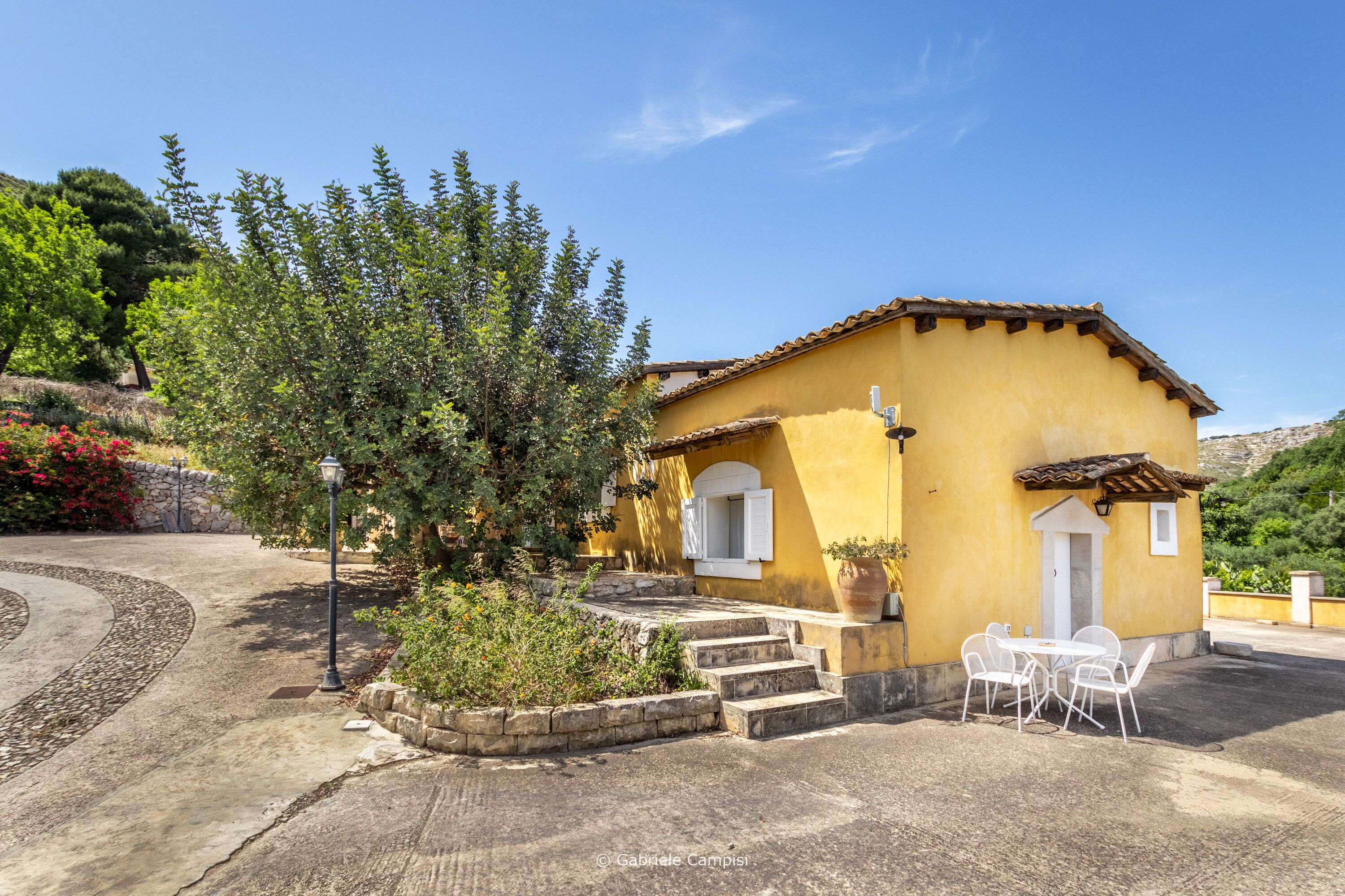 A yellow building with a tiled roof, a small porch, and a table with chairs.