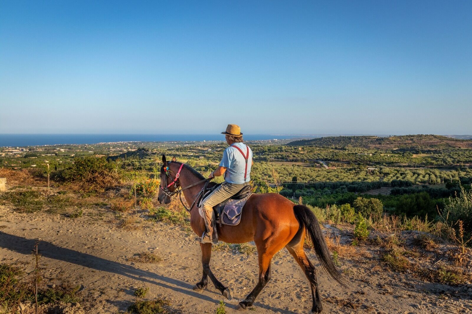 A person riding a horse on a dirt path with a view of a coastal landscape.