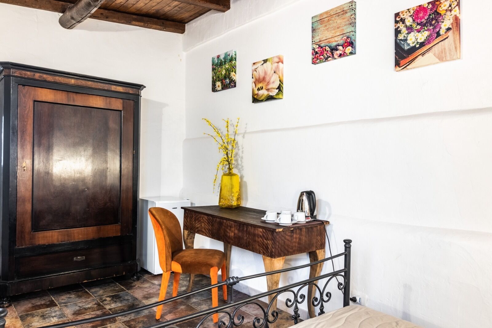 Une pièce d’angle avec un meuble en bois, un bureau agrémenté d’un vase de fleurs, une chaise et une machine à café.