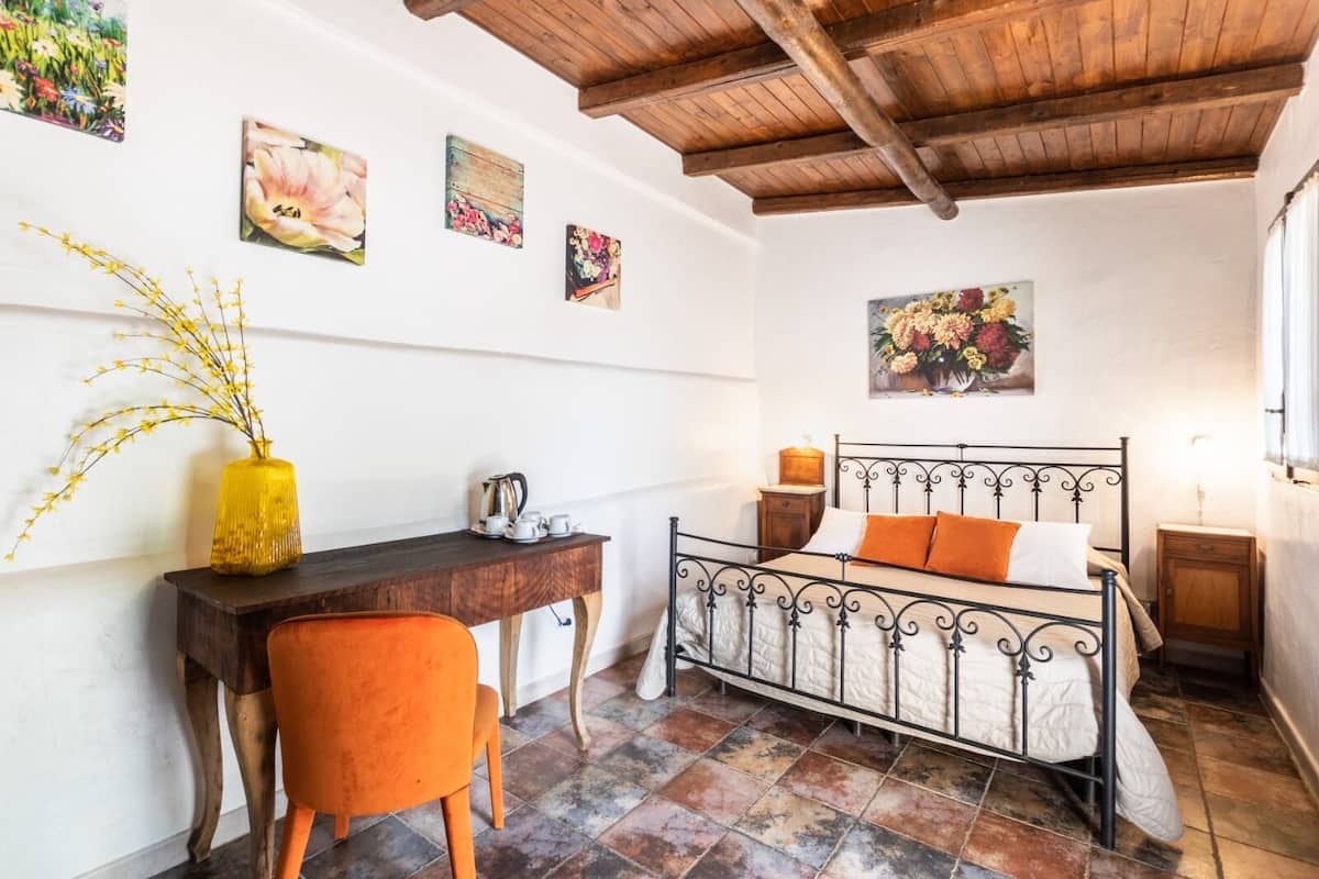Een slaapkamer met een bed, een bureau, een stoel en een bloevas.