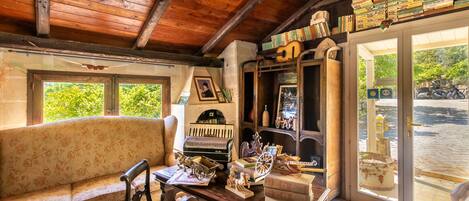 A cozy room with a wooden ceiling, a bench, a table with various items, and a door leading outside.